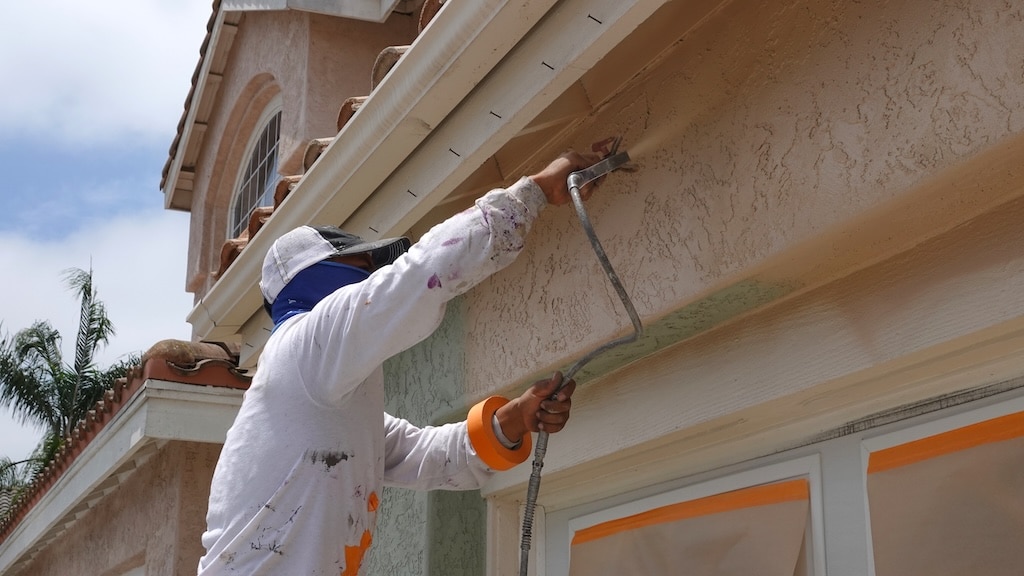 Professional contractor using a spray paint gun to paint the stucco on a home